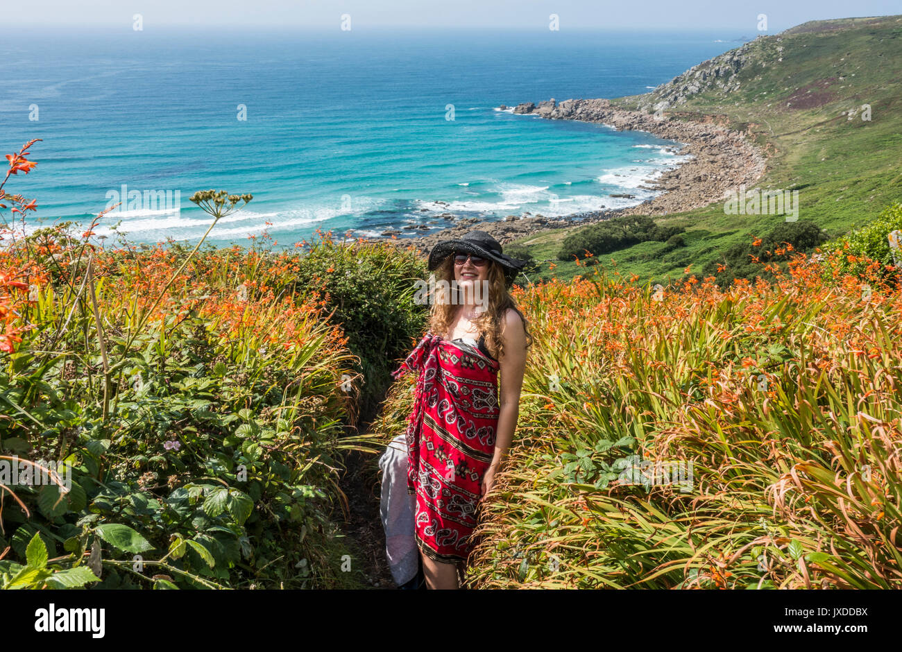 A pretty young woman, wearing a sarong and hat, standing on a narrow path leading down to Gwynver beach, Cornwall, England, UK. Stock Photo