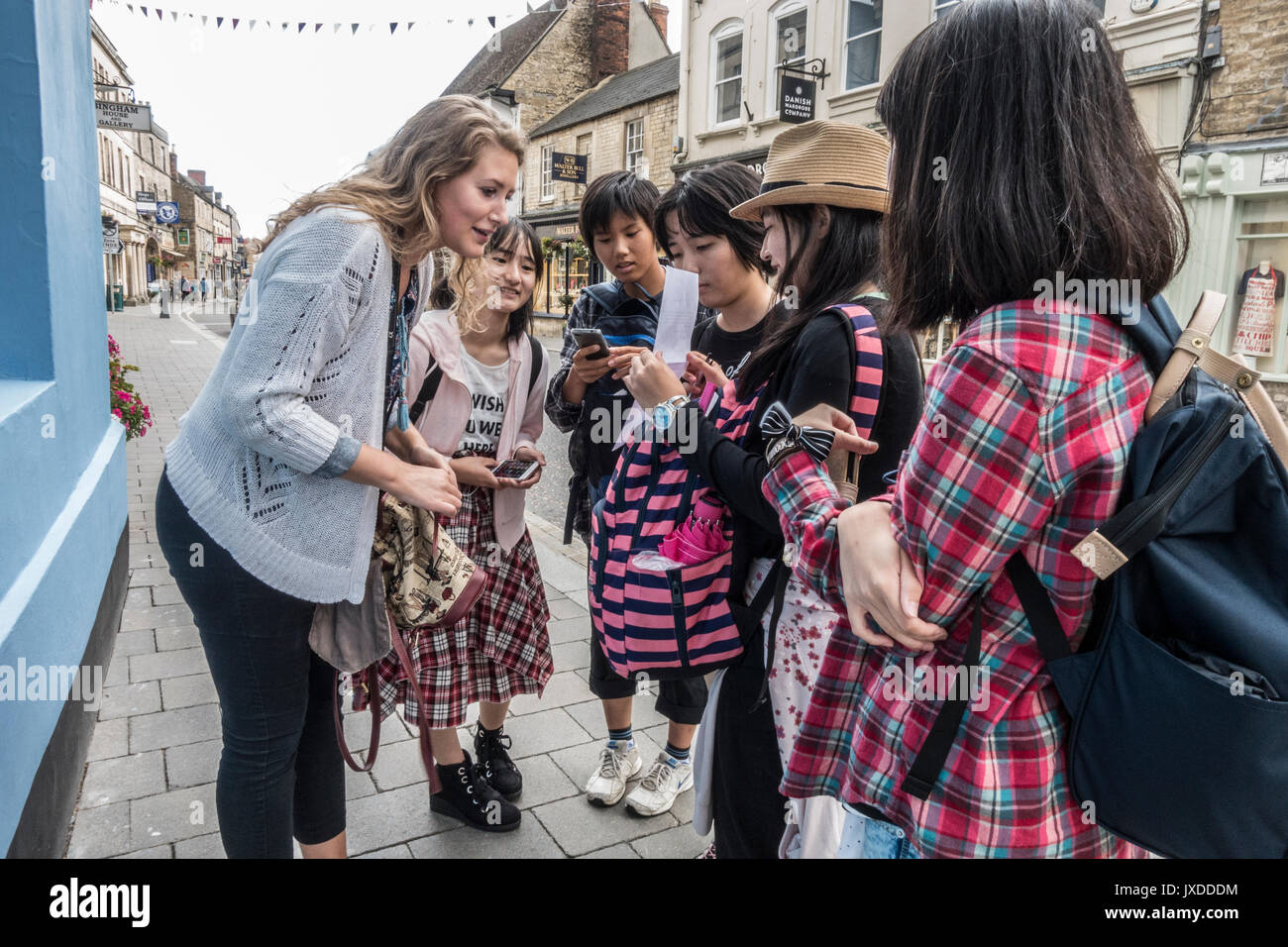 A pretty young English woman being asked for local information by a group of Japanese tourists, centre of Cirencester, Gloucestershire, England, UK. Stock Photo