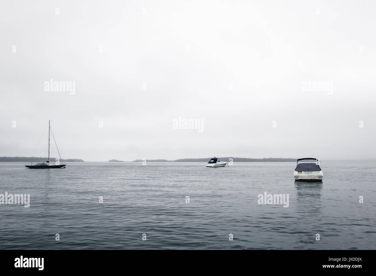 3 boats on the water between Sag Harbor and Shelter Island on a foggy, gray day in the Hamptons, NY. Stock Photo