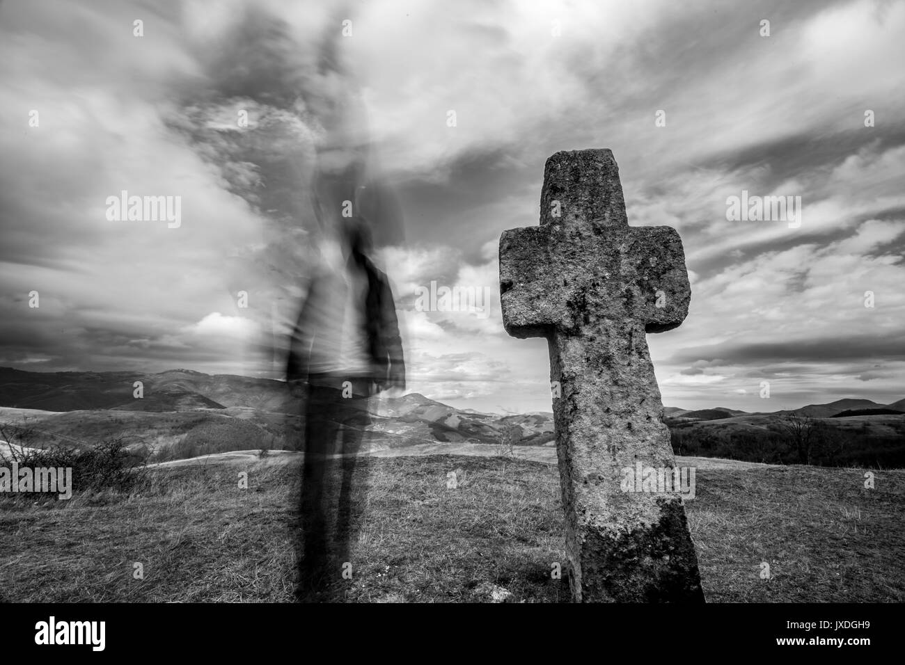 Ancient Christian stone cross and blurred silhouette of man Stock Photo