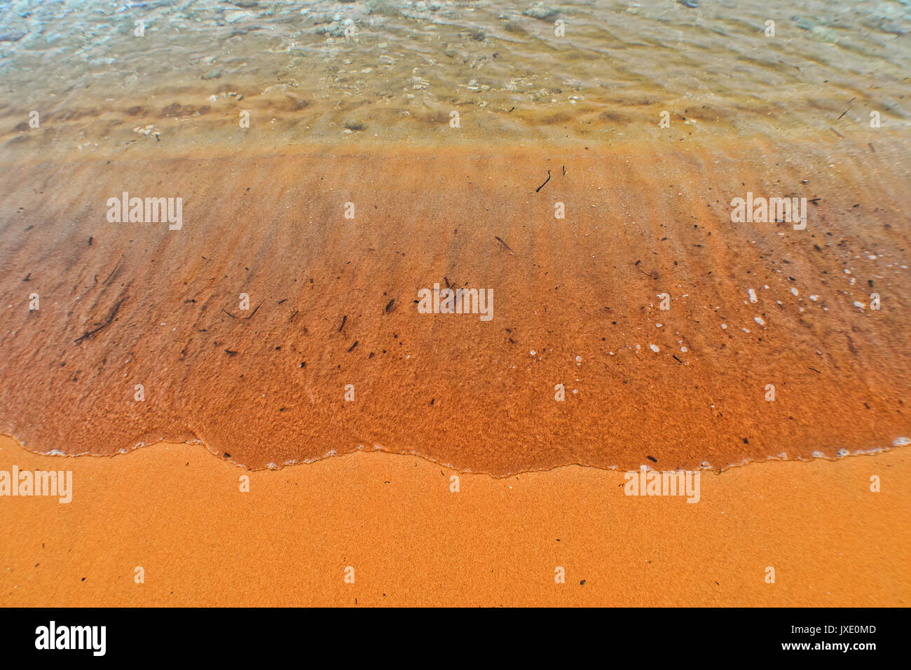 Sea lapping gently on an orange beach sand Stock Photo