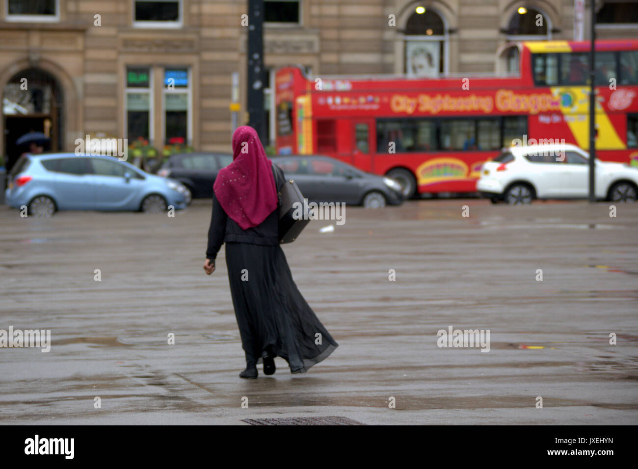 rainy day George square Glasgow young Asian woman with red burgundy hijab scarf viewed from behind wet street Stock Photo