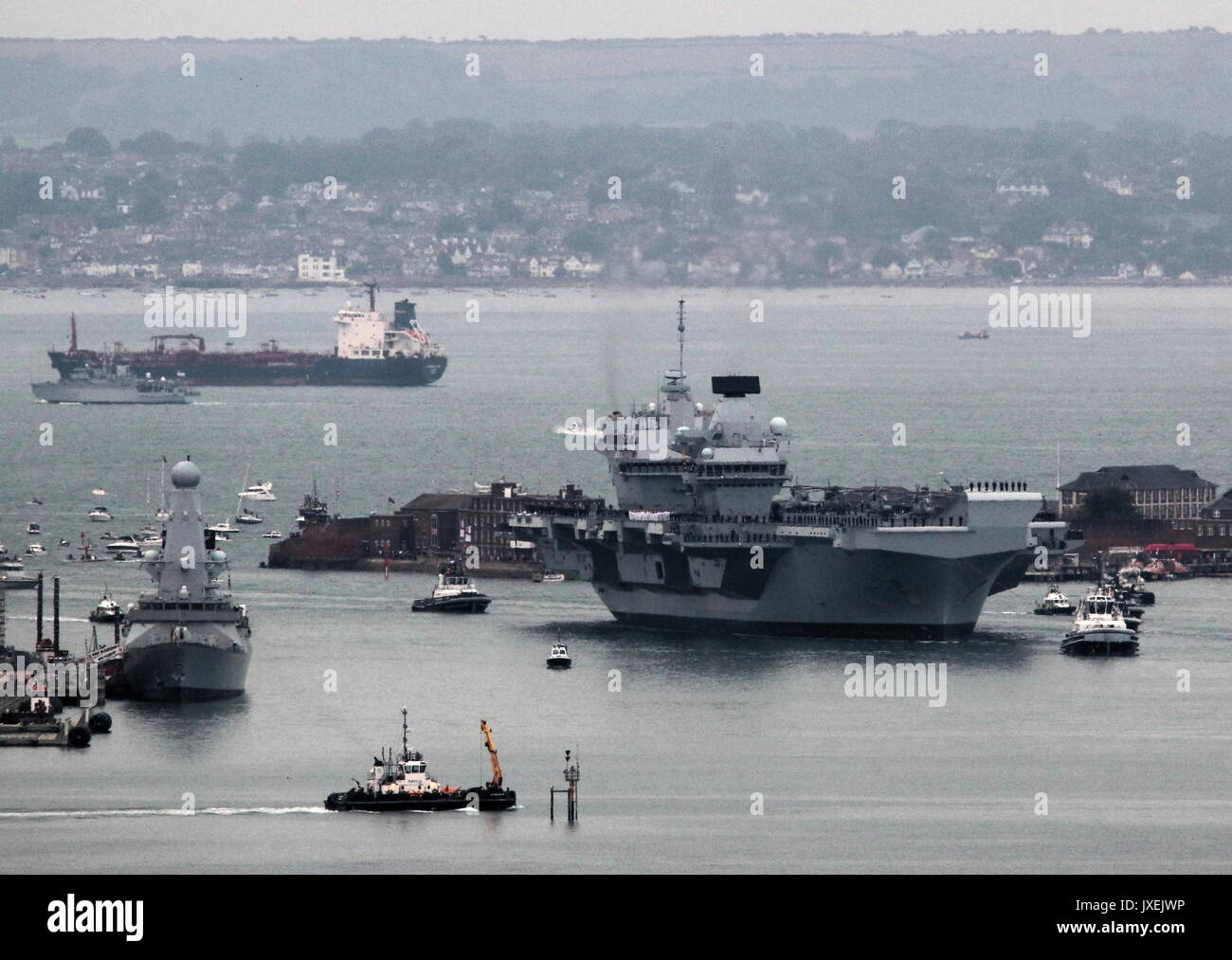 Portsmouth, UK. 16th August, 2017. - Royal Navy's biggest warship sails into home port - HMS Queen Elizabeth, the first of two 65,000 tonne, 900 ft long, state-of-the-art aircraft carriers sailed into Portsmouth Naval Base in the early hours of this morning, gently pushed and shoved by six tugs into her new berth on Princess Royal Jetty. The £3bn carrier, the largest warship ever built for the Royal Navy, arrived at her home port two days ahead of her original schedule.  Photo:Steve Foulkes/Ajax/Alamy Live News. Stock Photo