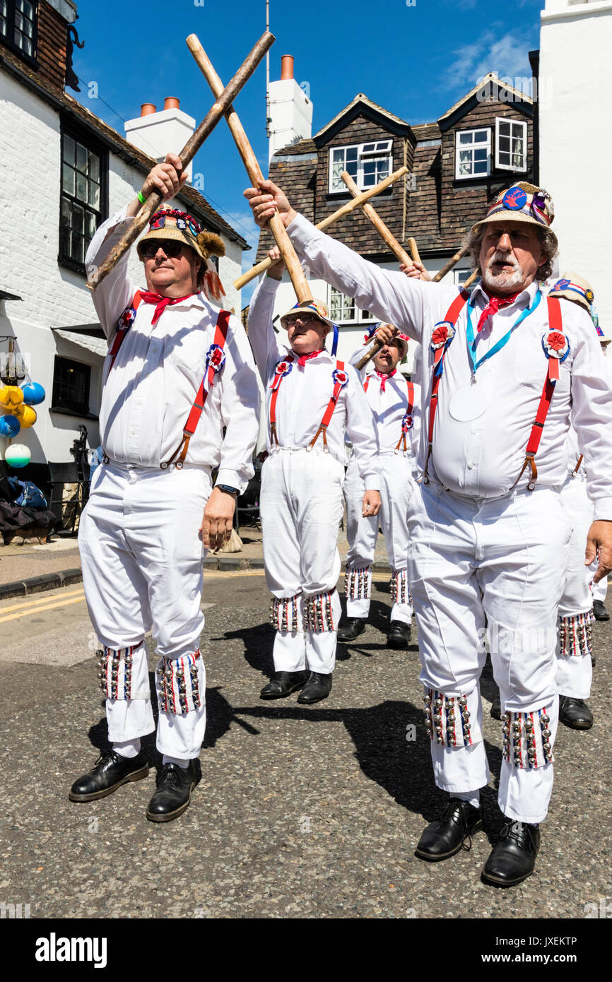 Traditional English Morris men from Hartley Morris dancers outside of the Old Curiosity Shop at the yearly Broadstairs Folk Week. Dancing in two rows wearing white trousers and shirts with straw hats, holding wooden poles. Stock Photo