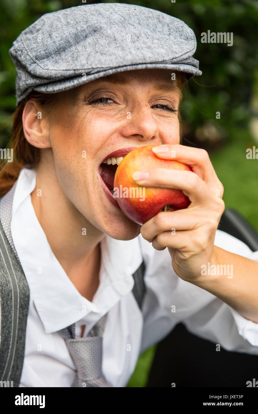 Red Haired Woman With Cap In The Garden Bites In An Apple Stock