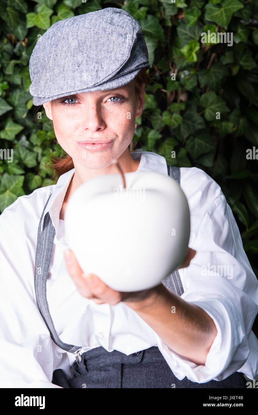 red-haired woman with cap in the garden offers apple Stock Photo
