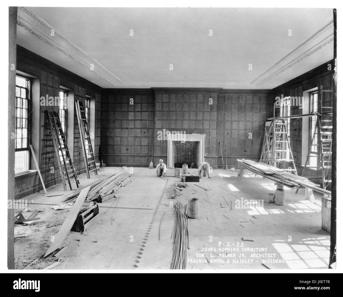 Alumni Memorial Residences Interior of AMR, Unidentifed room, Two workers are laying floor tiles, Room has a fireplace and woodpaneling on the walls, 1923. Stock Photo