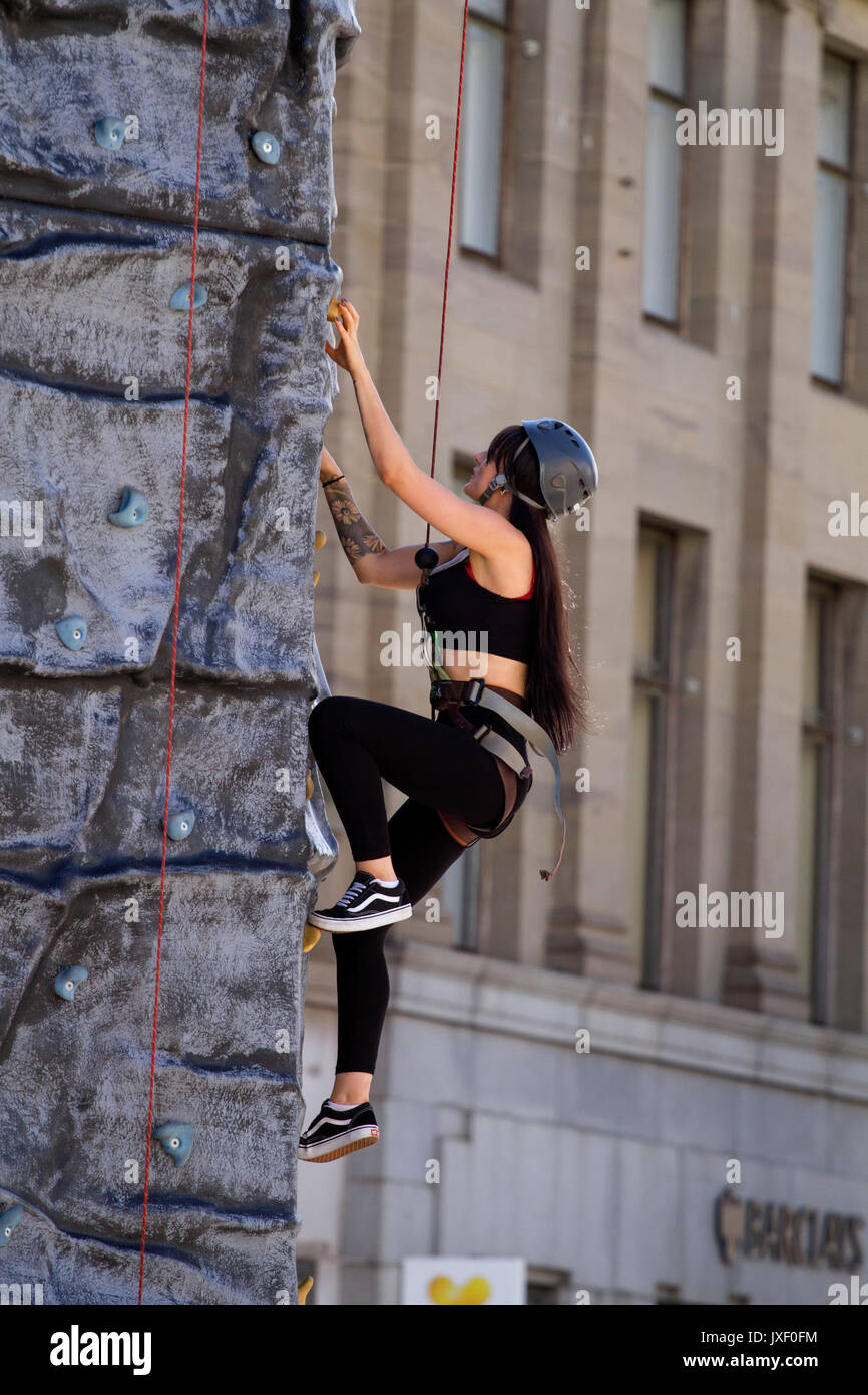 A beautiful athletic woman with long brown hair climbing up an artificial rock climbing wall in Dundee city centre, UK Stock Photo