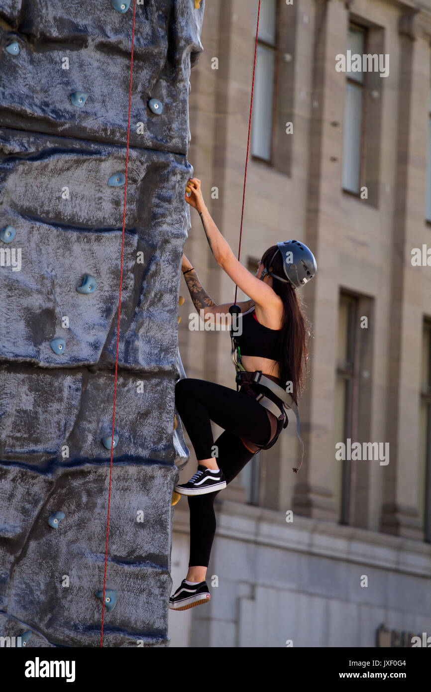 A beautiful athletic woman with long brown hair climbing up an artificial rock climbing wall in Dundee city centre, UK Stock Photo