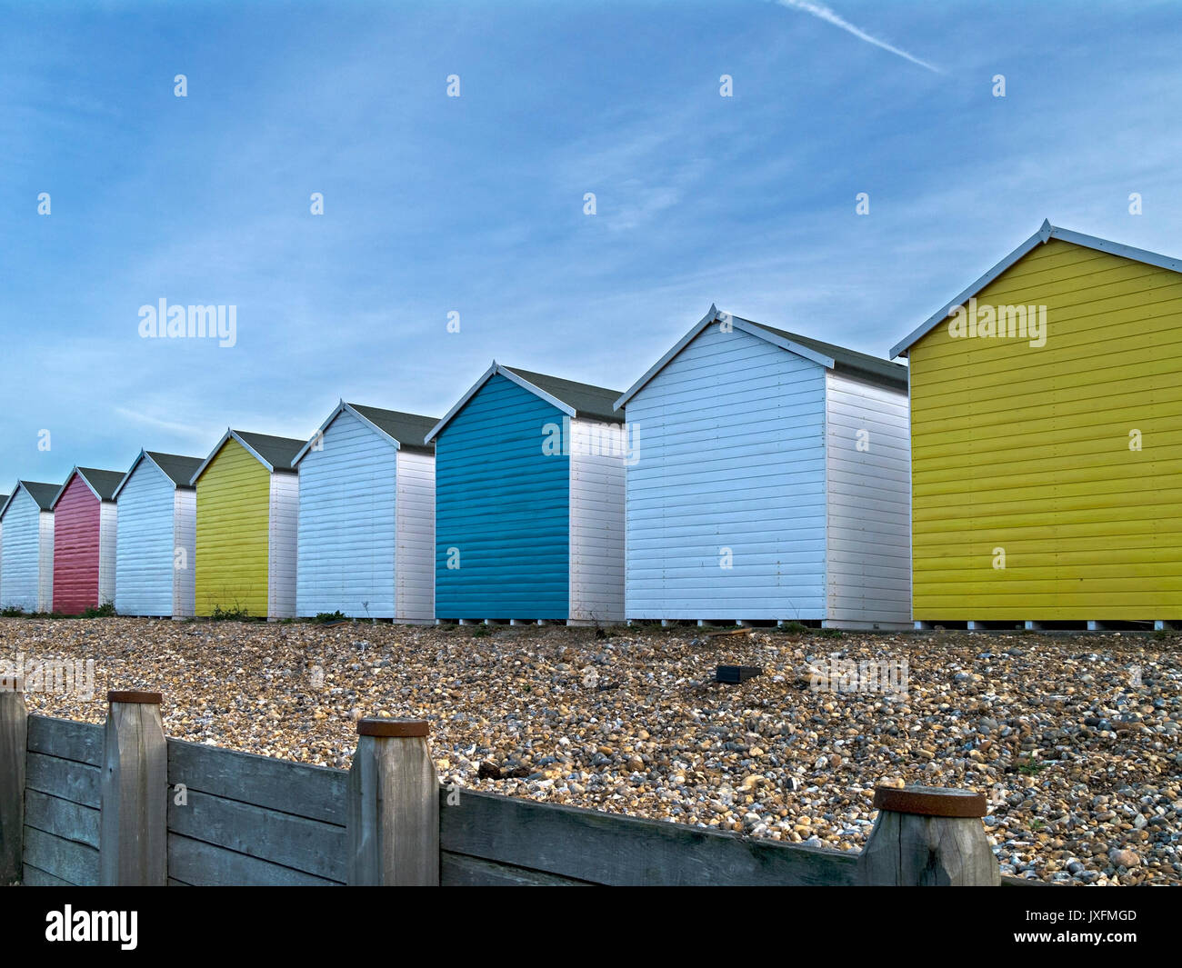 Row of brightly painted colourful wooden beach huts on Eastbourne shingle beach with blue sky above, Eastbourne, East Sussex, England, UK Stock Photo