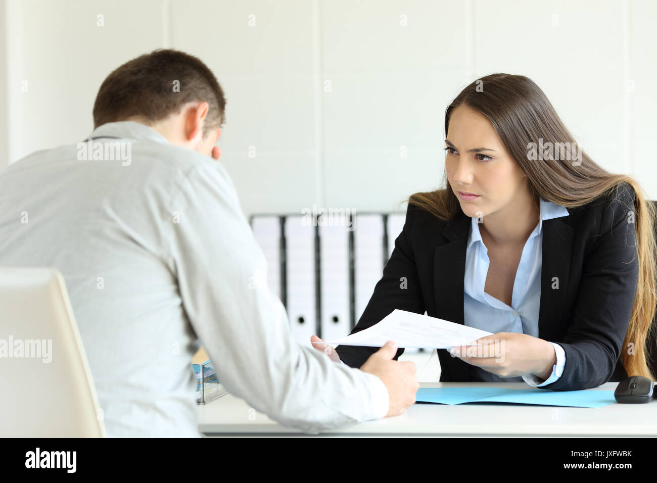 Angry boss giving a document to a sad employee sitting in a desk at office Stock Photo