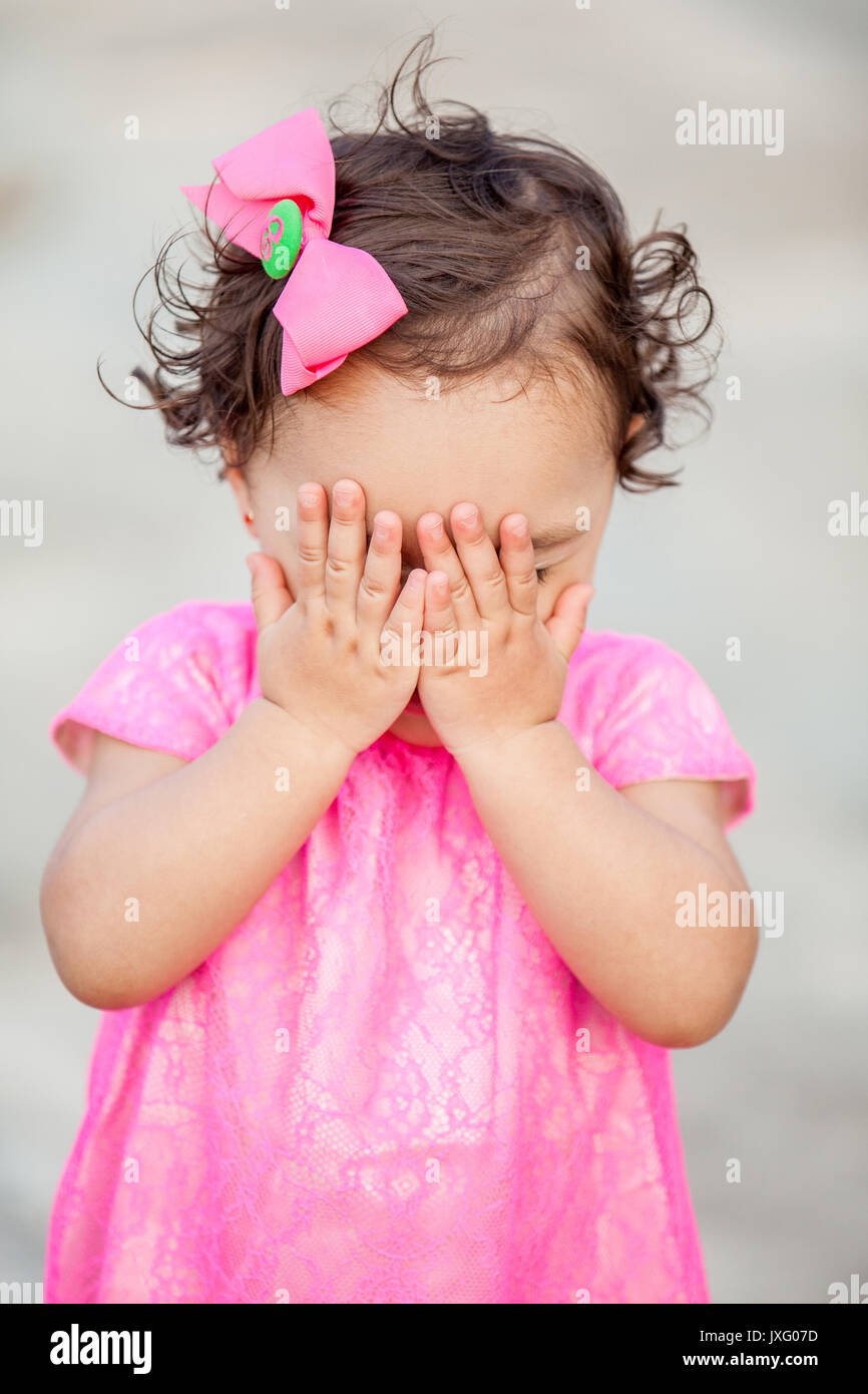 Baby girl hiding behind her hands playing peek a boo Stock Photo