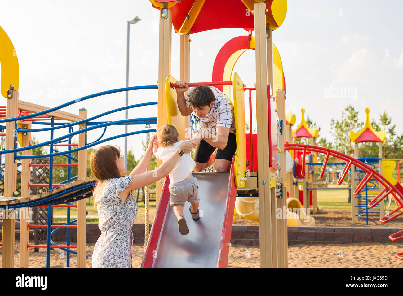playful child with parents at the playground outdoor. Mom, dad and ...