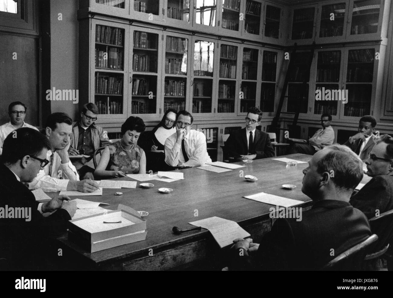 Economics, Classes, Carl Christ, African American Students, Candid shot taken during an economics seminar, Students are sitting around a large desk, listening and taking notes during the lecture, 1963. Stock Photo