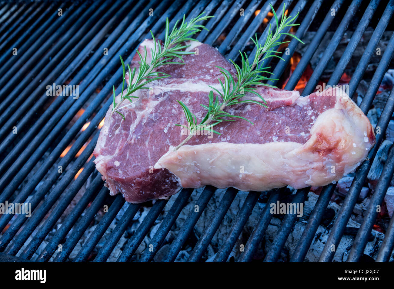 Tbone steak cooking on an open flame grill , with rosemary and salt
