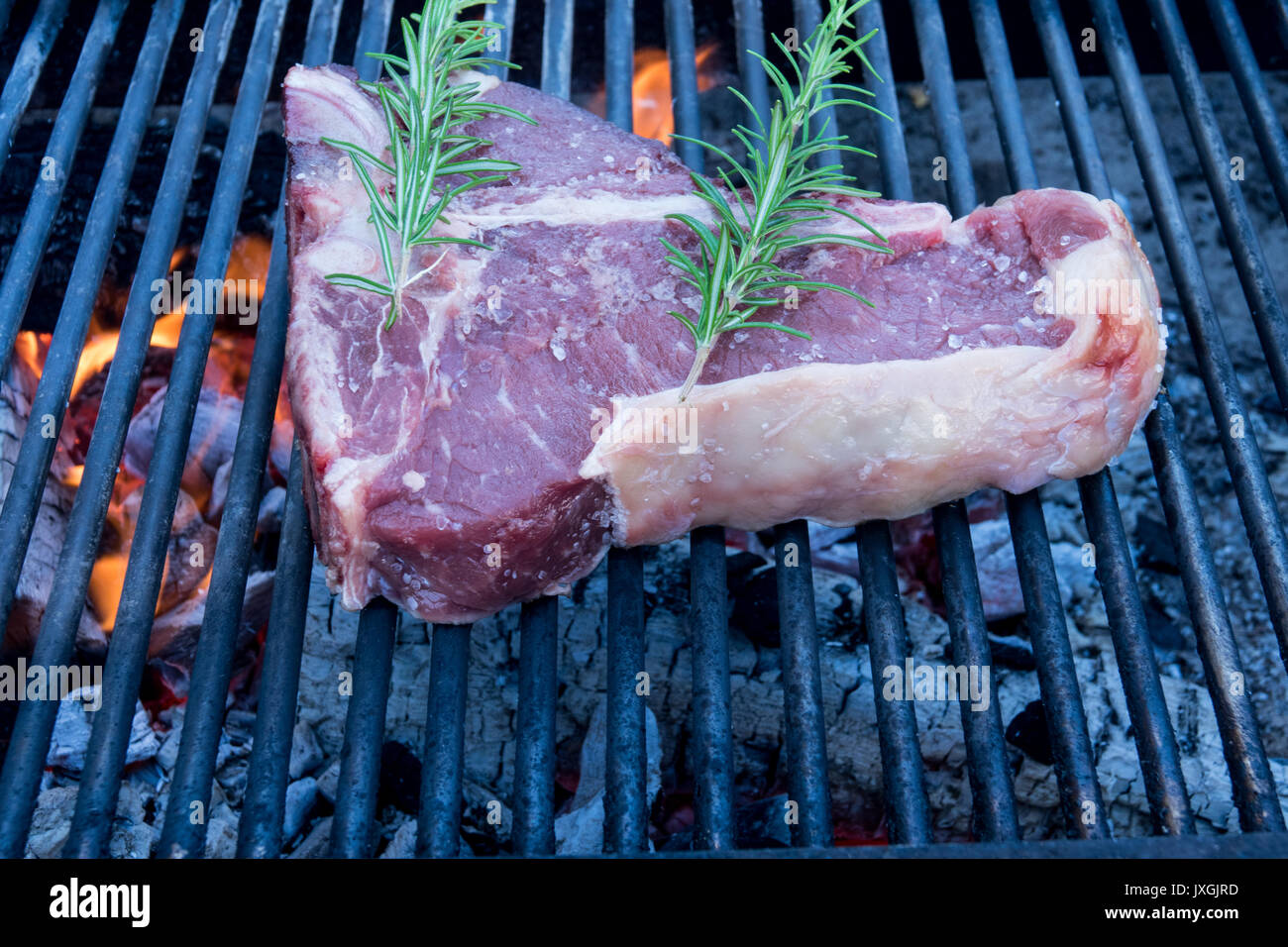 Tbone steak cooking on an open flame grill , with rosemary and salt