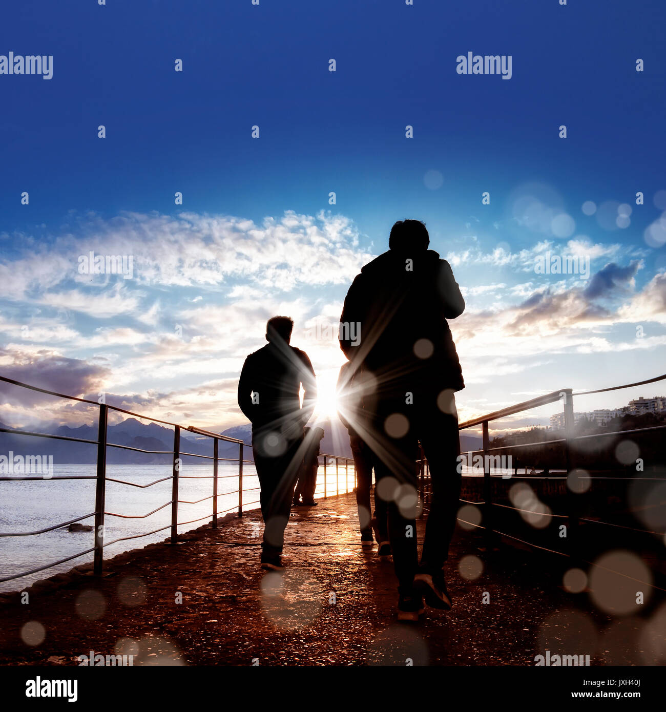 silhouetted people walking on street over sunset sky with sunbeam Stock ...