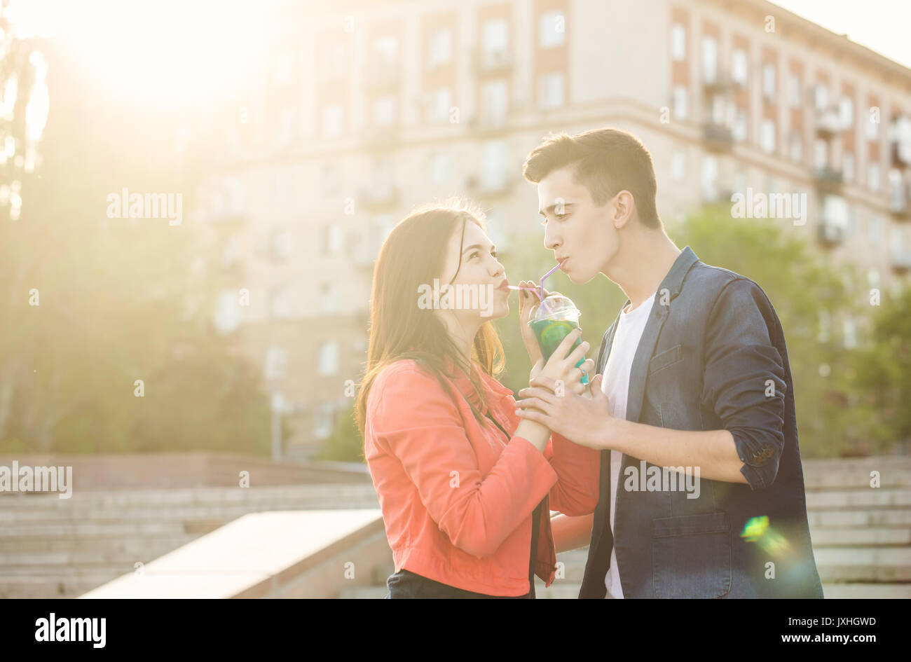 Teens drink fresh fruit from the cups. They drink from one glass. A couple in love on a date. Romance of first love. Stock Photo