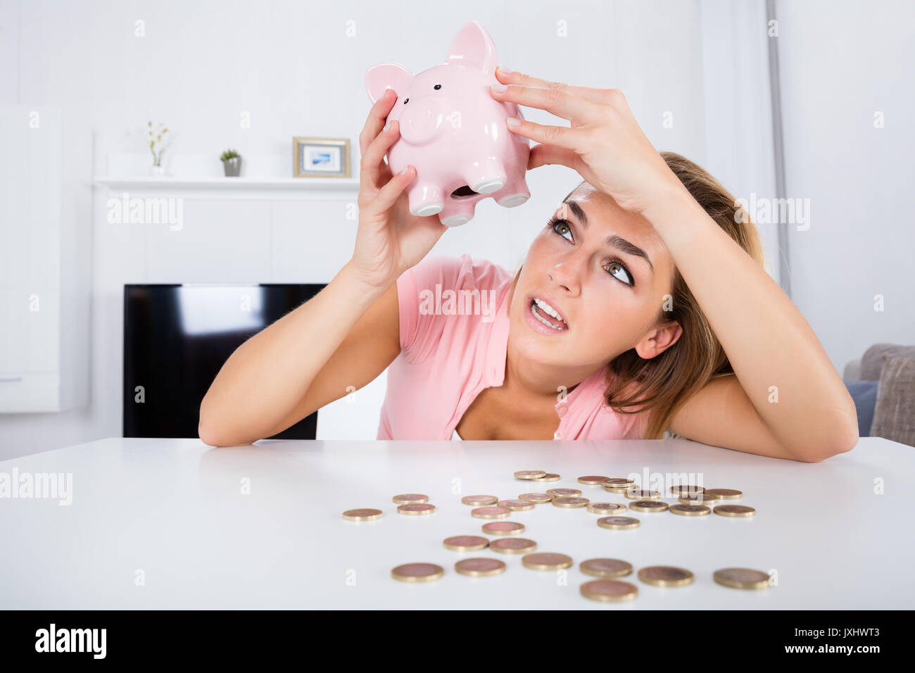Young Unhappy Woman Emptying Her Piggybank Savings With Less Than Expected At Home Stock Photo