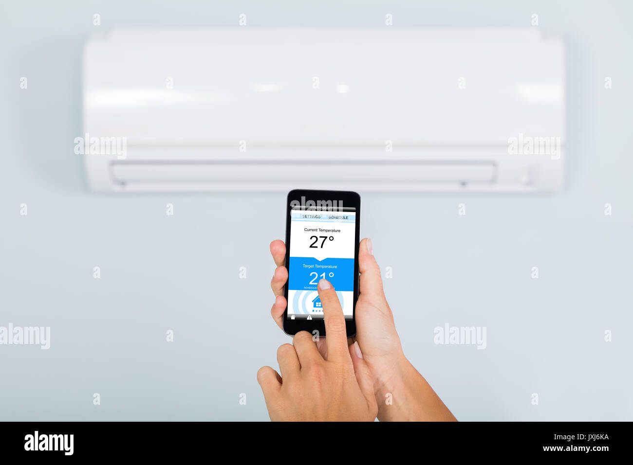 Woman Hand Setting Temperature Of Air Conditioner Using Smartphone App At Home Stock Photo