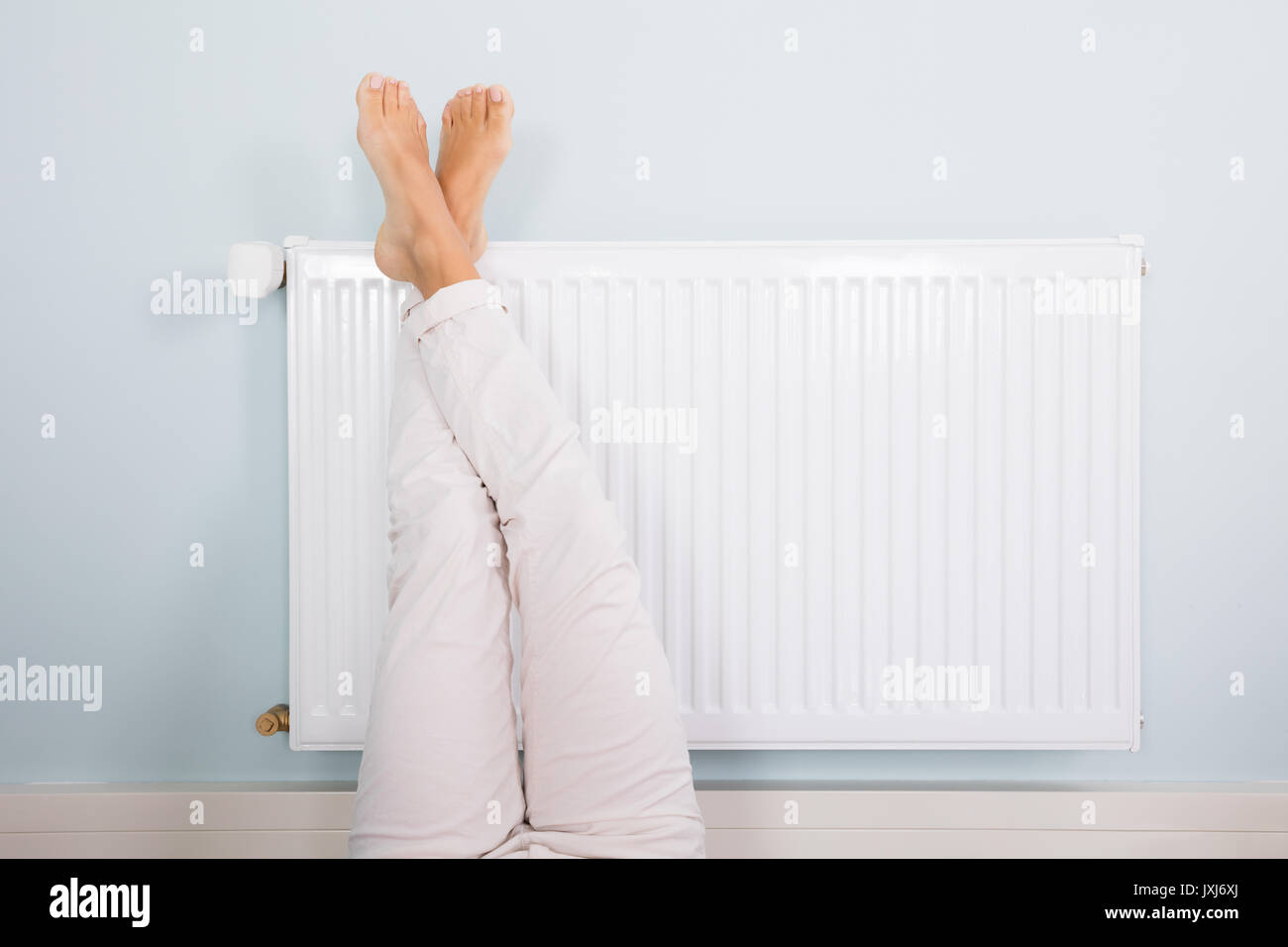 Woman Warming Up Her Feet On White Radiator At Home Stock Photo