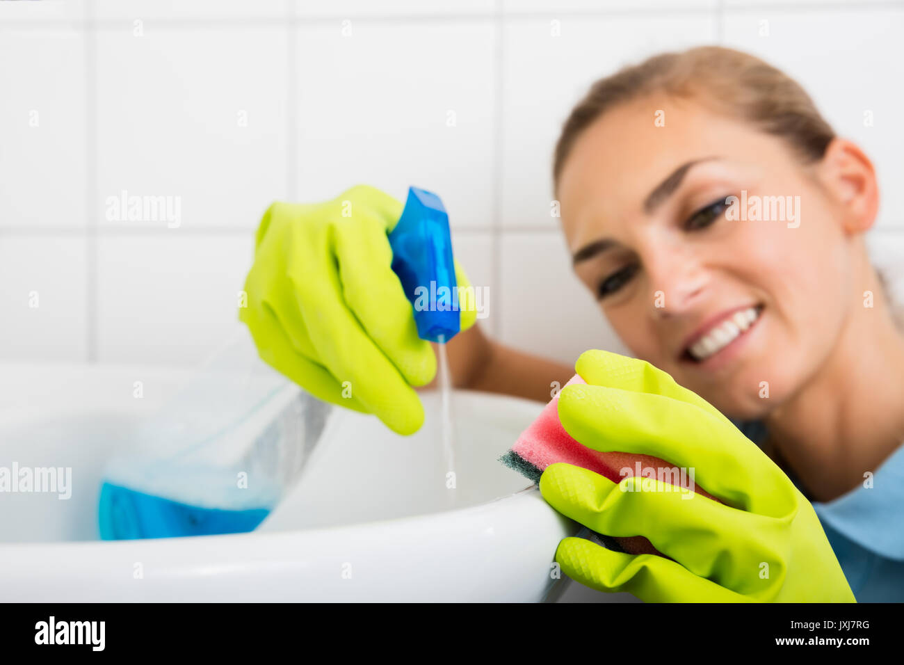 Close-up Of Smiling Woman Cleaning The Basin With Spray Bottle And Sponge In The Bathroom Stock Photo