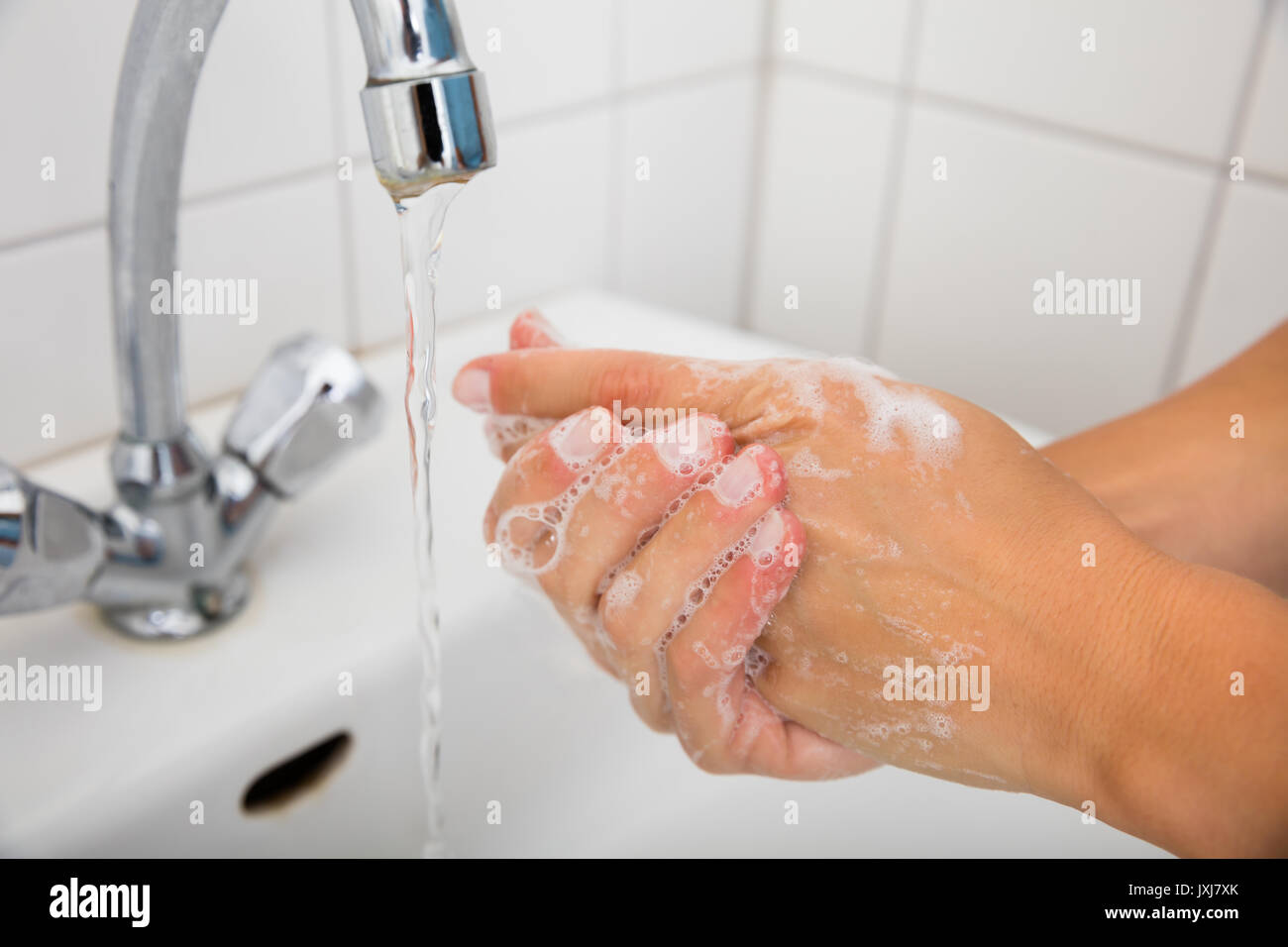 Close-up Of Woman Applying Soap While Washing Hands In Basin With Open Tap Stock Photo