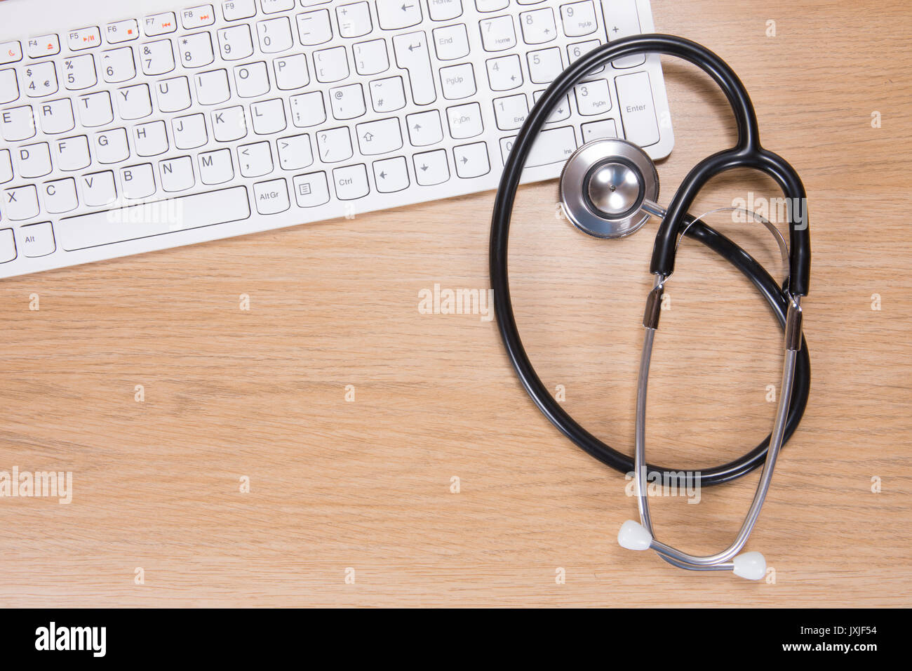 High angle view of acoustic stethoscope with computer keyboard lying against wooden background Stock Photo
