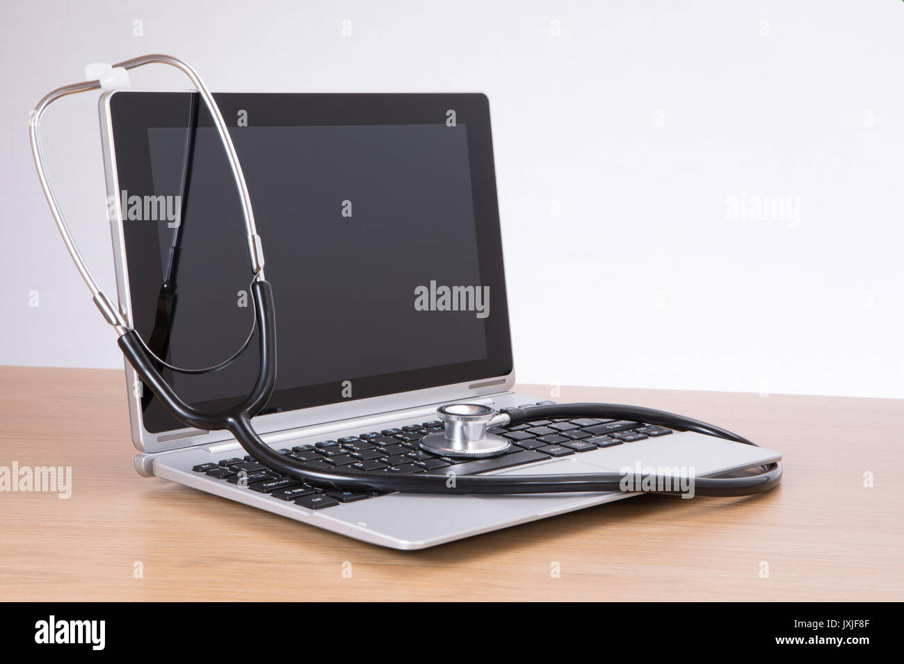 Acoustic stethoscope hanging over laptop screen against wooden desk Stock Photo