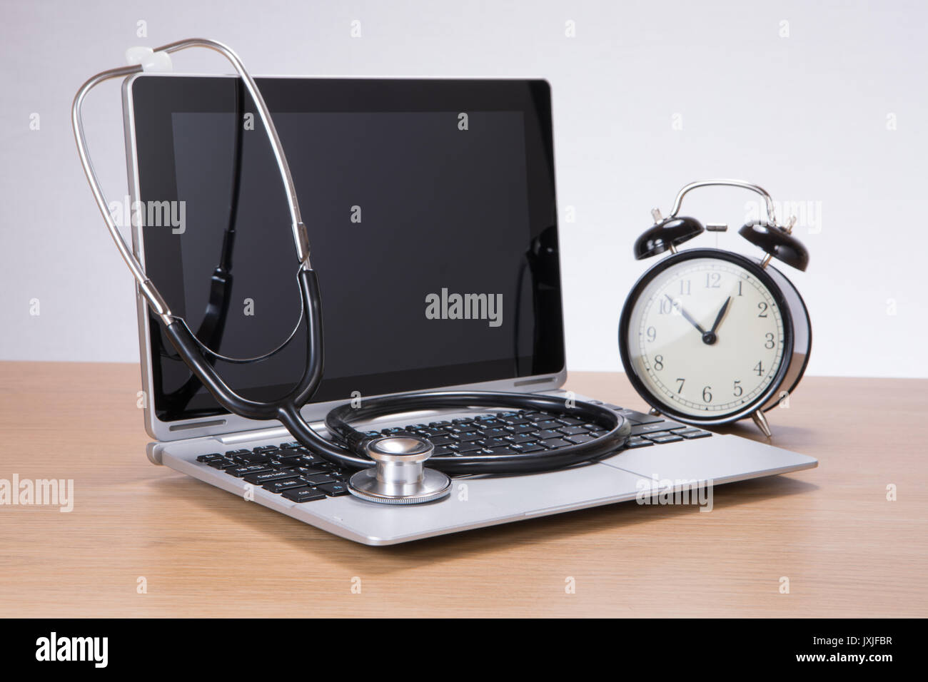 Side view of black and silver medical stethoscope on laptop computer next to black and white alarm clock Stock Photo