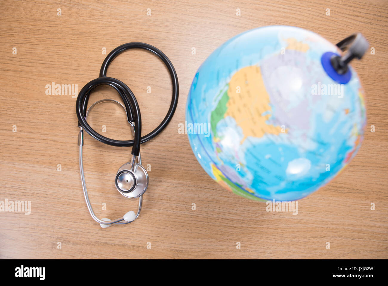 High angle view of acoustic stethoscope lying next to globe against wooden background Stock Photo