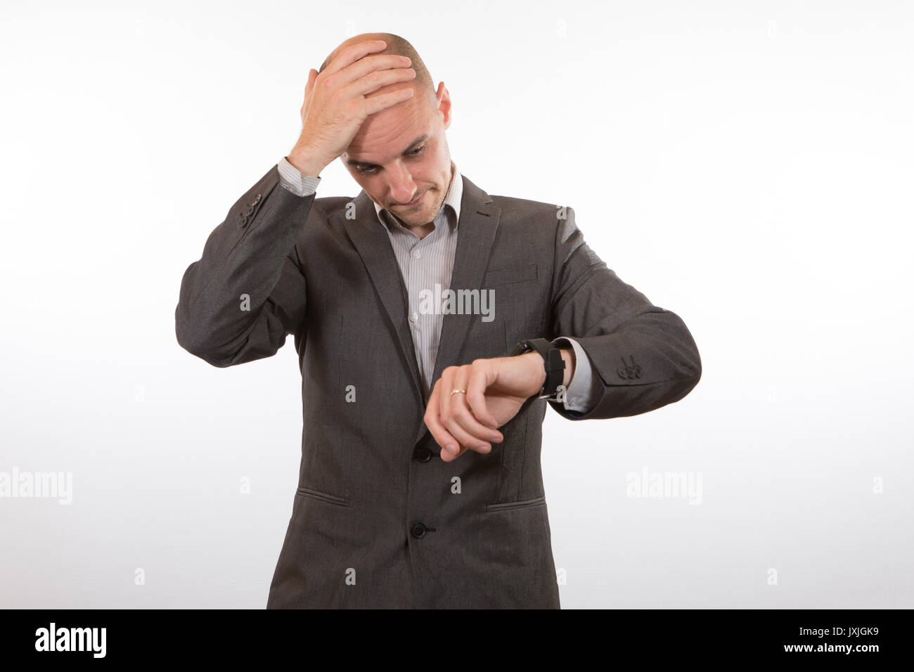 Forgetful businessman looking at his watch in dismay with his hand to his head and a wry smile as he realises he will be late Stock Photo