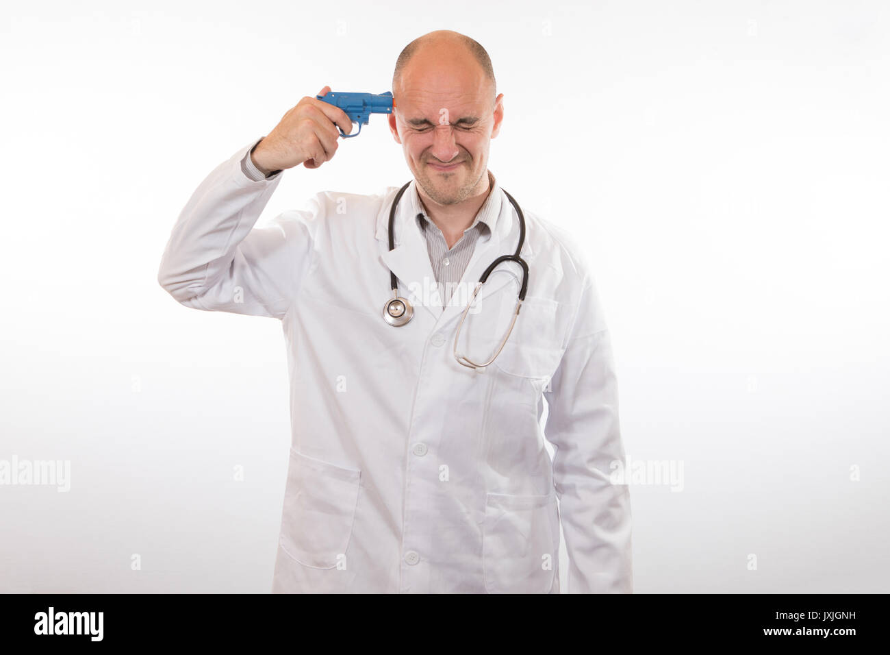 Anguished doctor holding a small blue toy plastic gun to his head with his eyes screwed shut isolated on white in a conceptual image Stock Photo