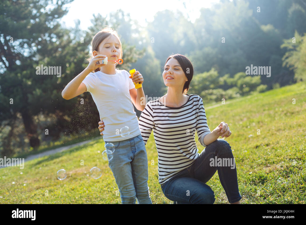 Loving mother watching her daughter play with soap bubbles Stock Photo