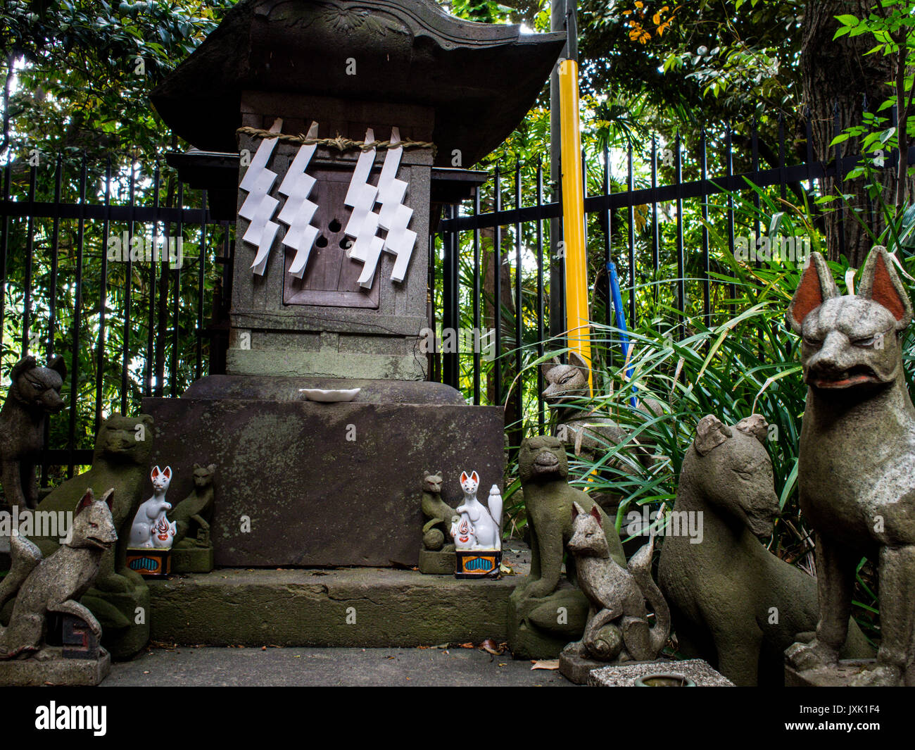 Kitsune fox guardians in front of Shinto shrine with shide zig zag paper streamers, Tamagawa Jinja, Setagaya, Tokyo Stock Photo