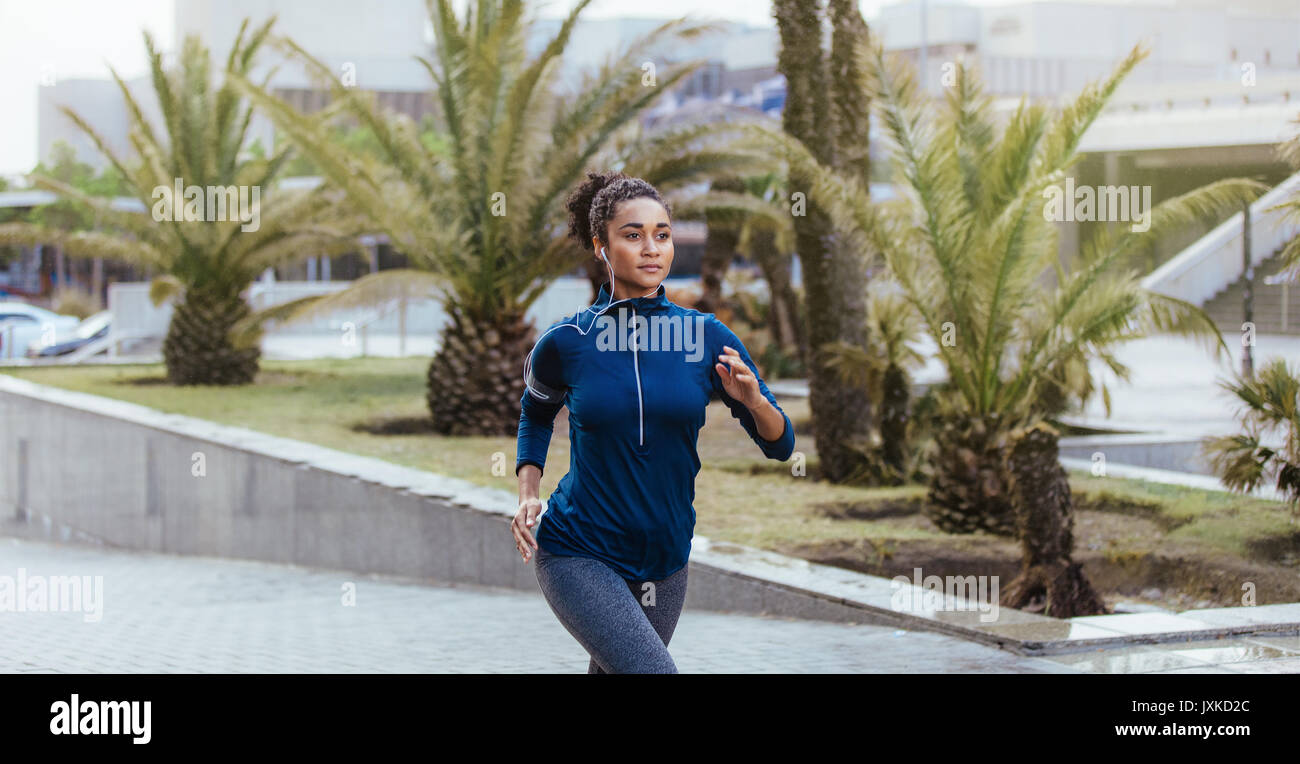 Woman runner in jogging outfit running on a street. Woman listening to  music using earphones while running Stock Photo - Alamy
