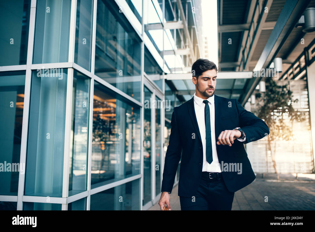 Business traveler checking time on his wristwatch at airport. Young businessman looking at his watch while walking inside public transportation buildi Stock Photo
