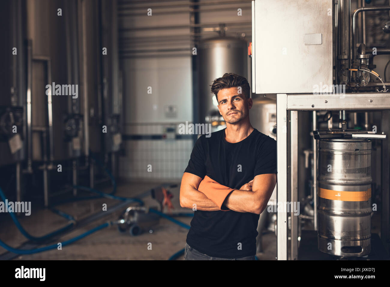 Portrait of young man standing by beer filling machine. Brewery worker with industrial equipment. Stock Photo