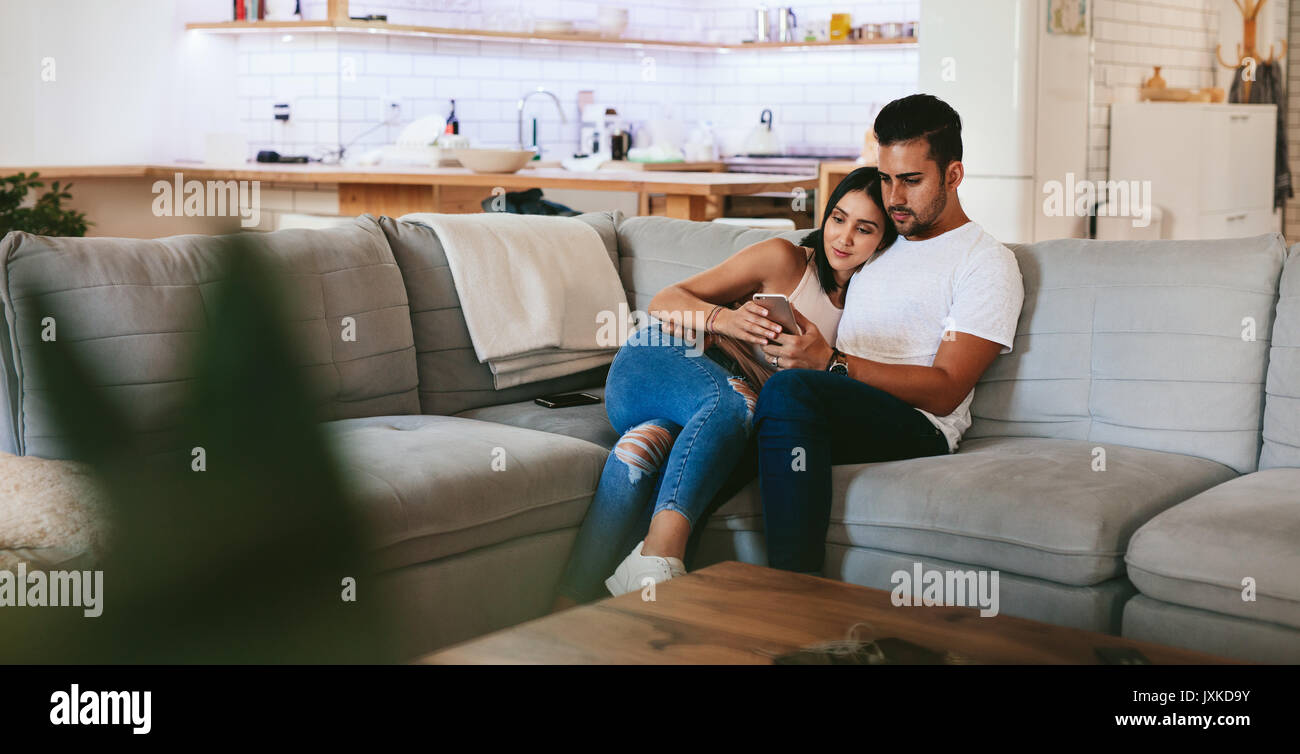 Young couple relaxing on couch with smartphone at home in the living room.  Man and woman sitting together in sofa and looking at mobile phone Stock  Photo - Alamy