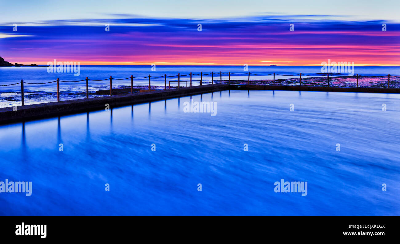 Bright Magenta and blue colours in the sky and blurred water at sunrise at Mona Vale rock pool of Sydney Australia Pacific coast. Stock Photo