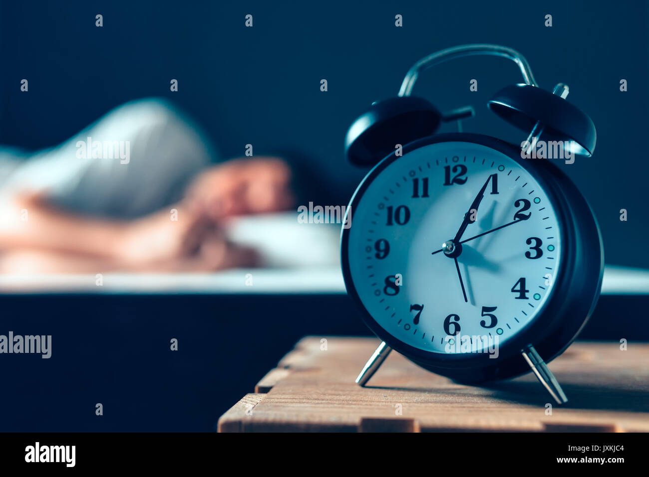 Sleeping disorder or insomnia concept, selective focus of vintage clock in bedroom and out of focus male person trying to fall asleep in bed Stock Photo