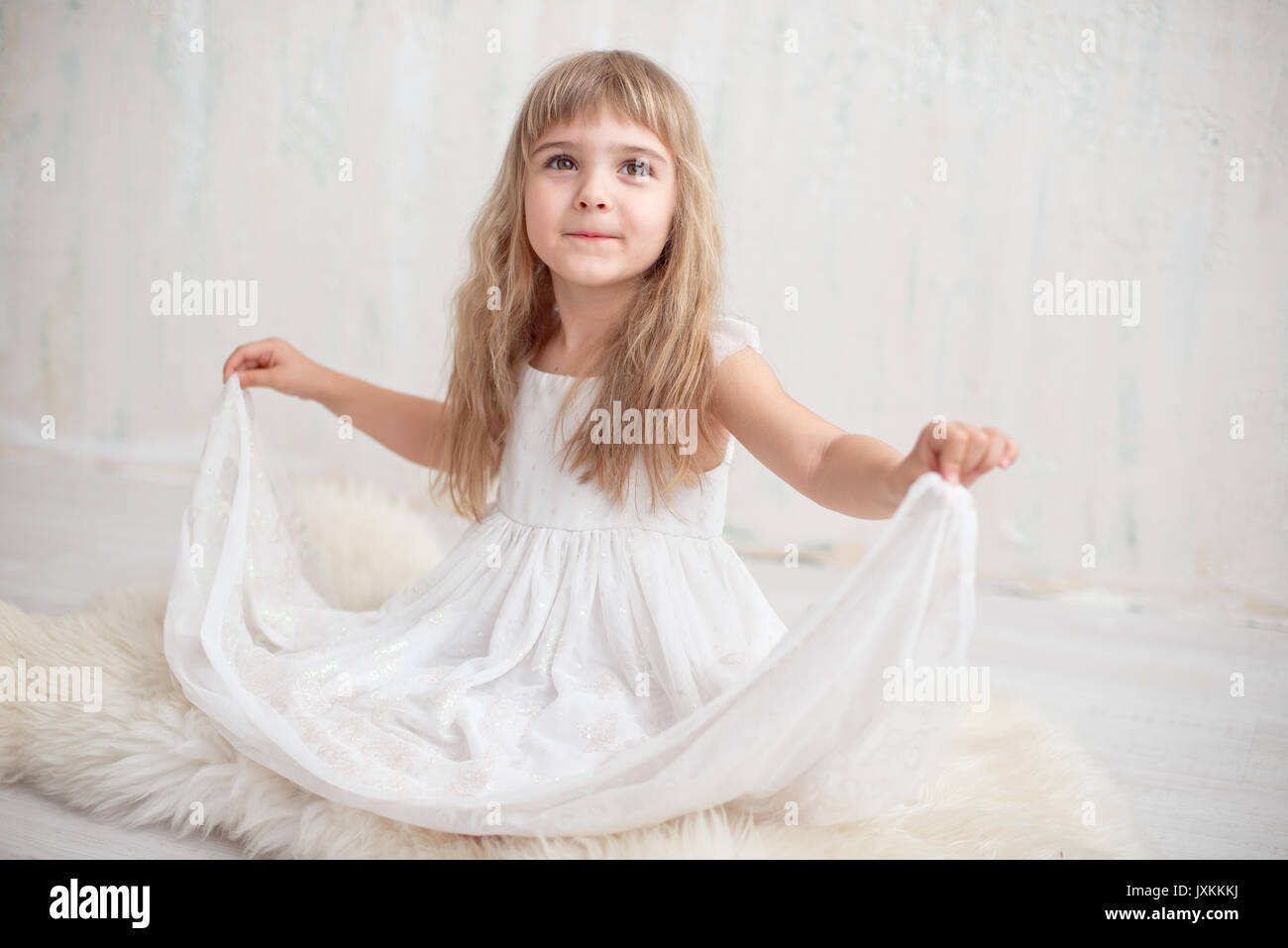 Portrait of pretty little girl in white dress , looking at camera and ...
