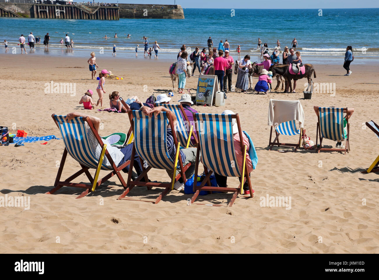 People visitors tourists sitting sat on deckchairs at the seaside sands at South Bay beach in summer Scarborough North Yorkshire England UK Britain Stock Photo