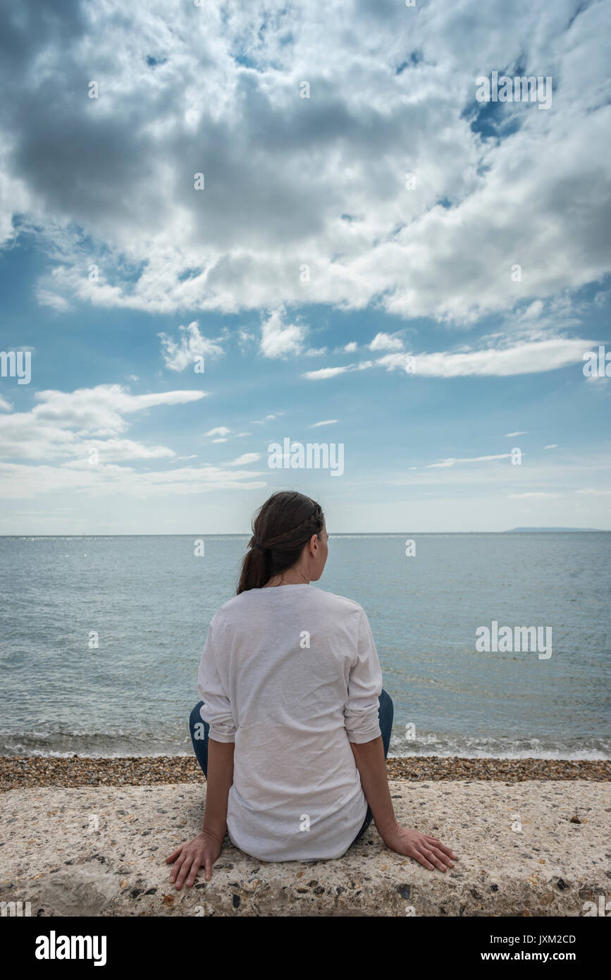 Back view of a woman sitting on a wall looking out to sea Stock Photo ...