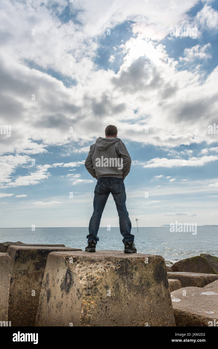 Back view of a man standing on rocks,  looking out to sea. Stock Photo