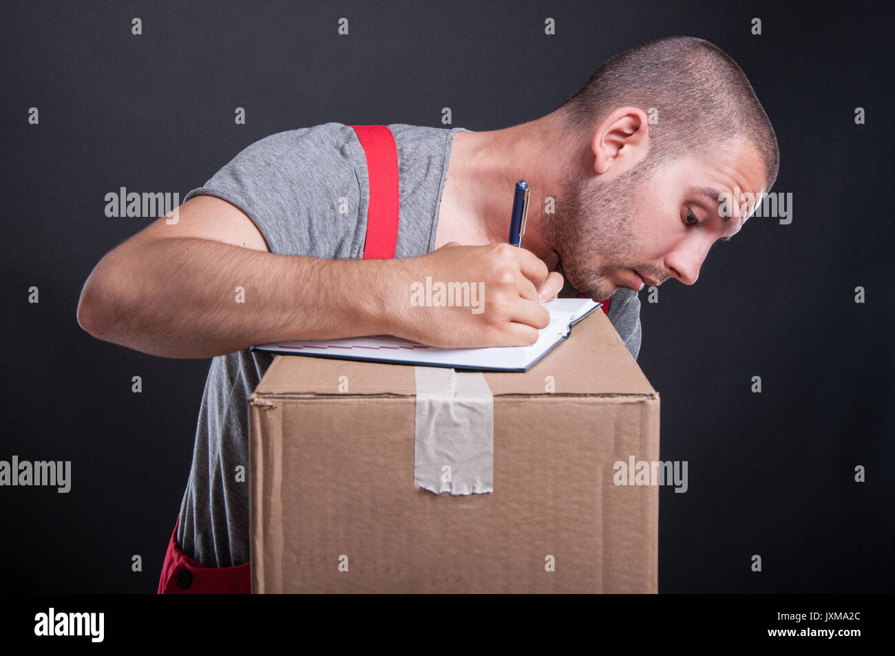 Mover guy taking notes from cardboard boxes on black background Stock Photo