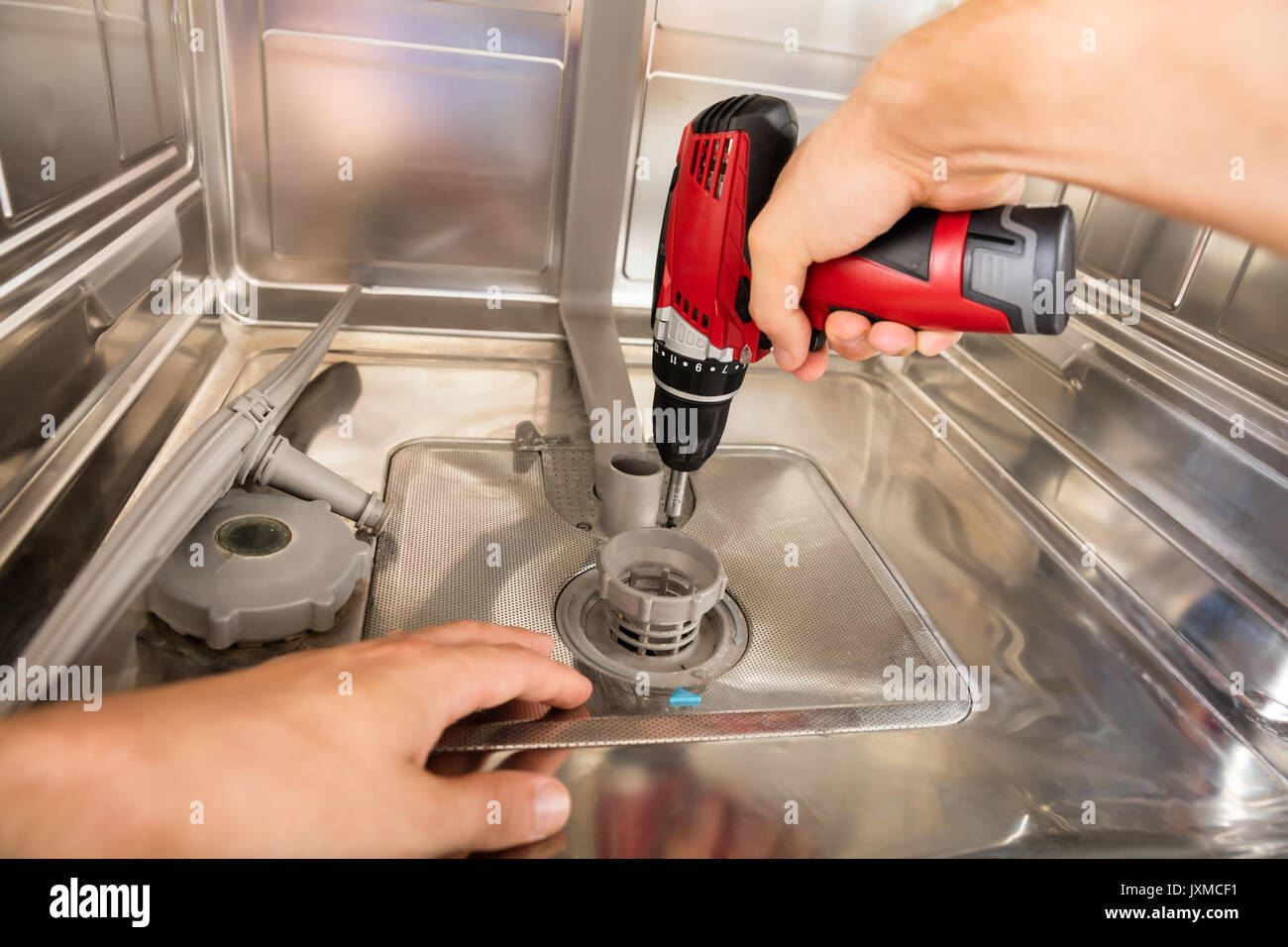 Closeup Of Repairman Fixing Dishwasher With Electric Drill Stock Photo