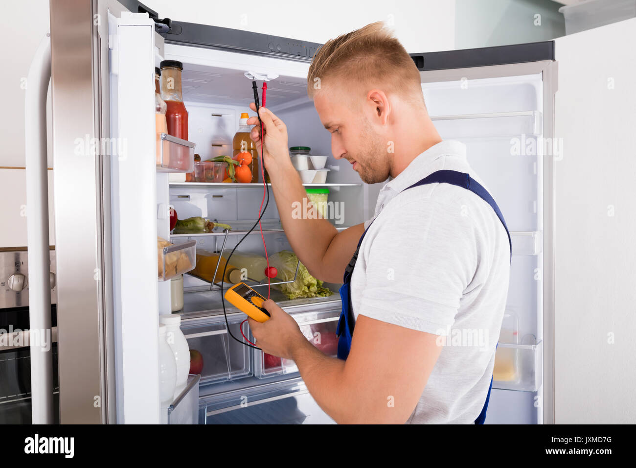 Young Repairman Checking Refrigerator With Digital Multimeter Stock Photo