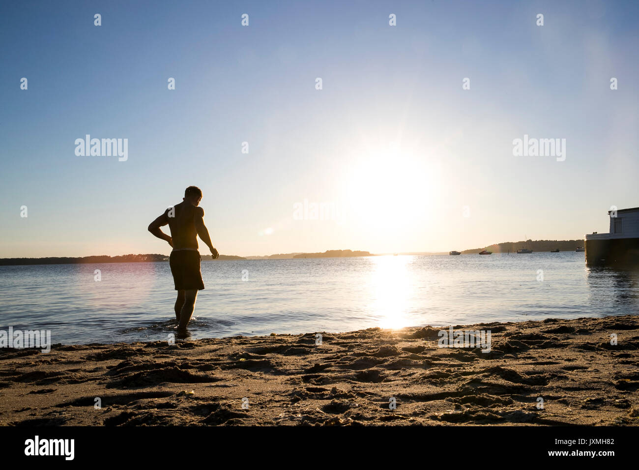 Backlit young male swimmer walking into sea at sunset Stock Photo