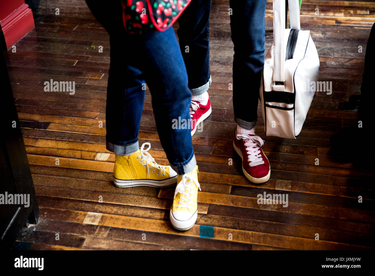 Jeans and trainers worn by couple standing on wooden flooring Stock Photo